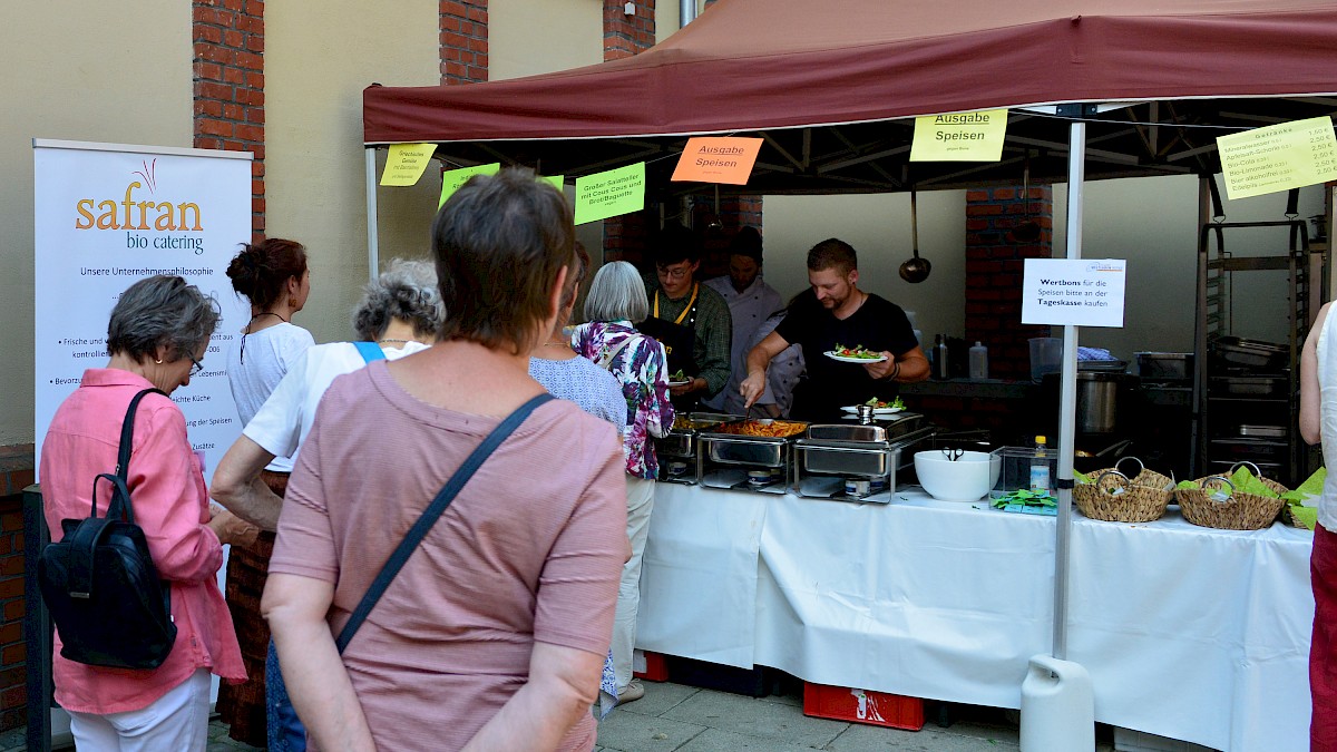 Einige Menschen stehen am Catering-Stand der Weltladen-Fachtage 2019 an. Dort wird das Mittagessen ausgegeben.
